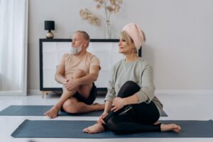 Senior couple doing yoga together on mats on tile flooring.